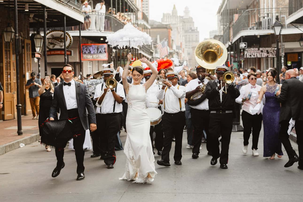 Bride and groom parading in the French Quarter with a brass band behind them during a wedding second line.