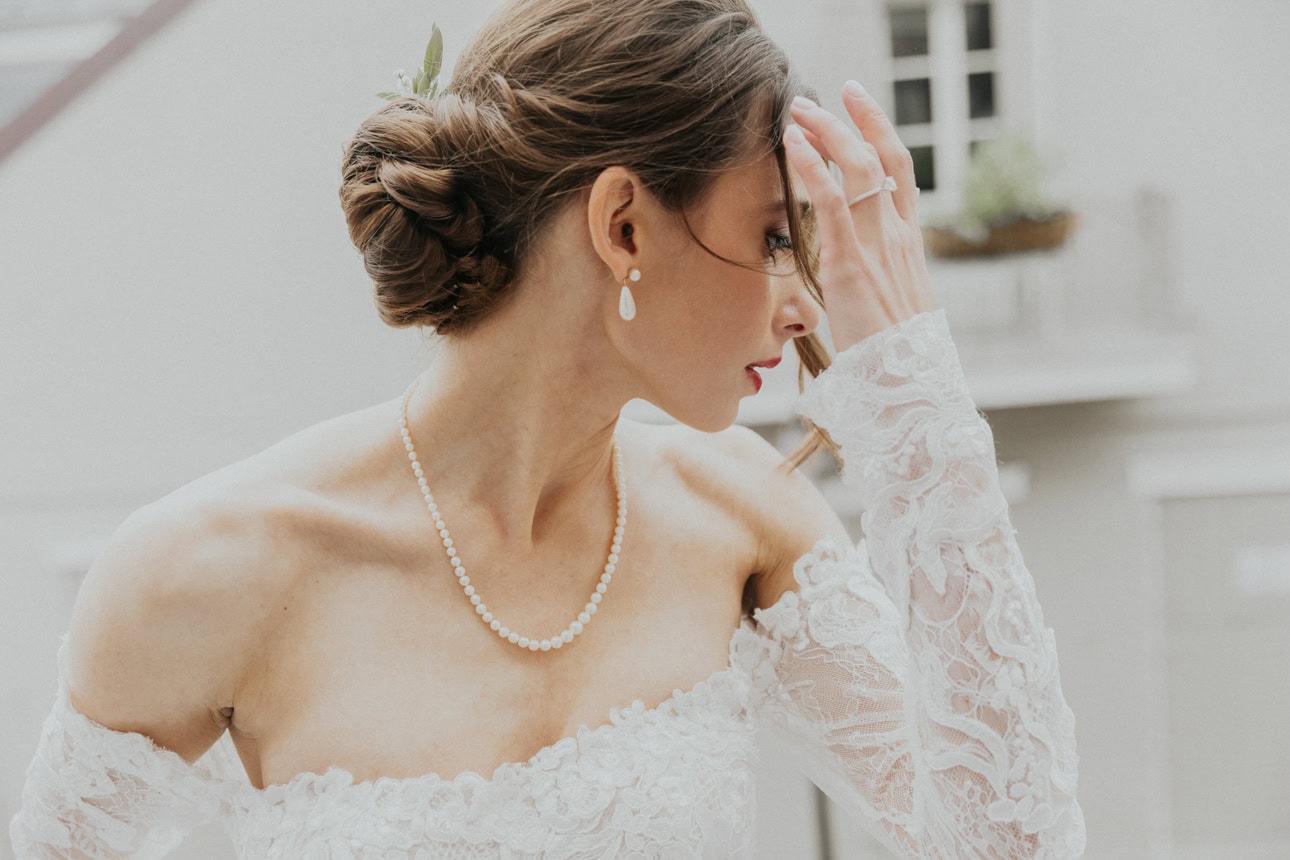 Bride in lace dress sweeps her bangs off her forehead looking down toward the street.