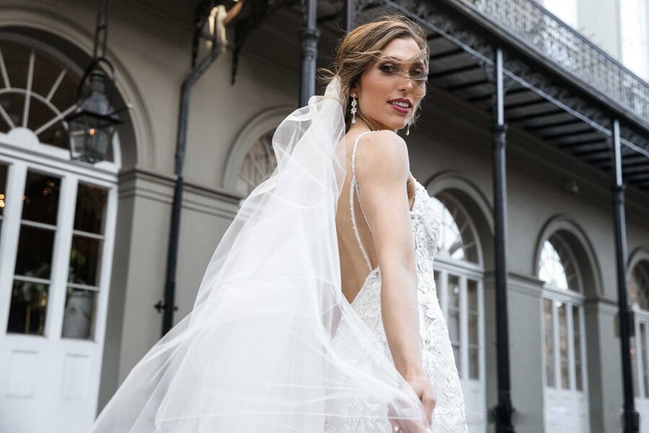 A bride on her wedding day, in the French Quarter looking back over her shoulder at her veil. Her hair whipping in the wind.