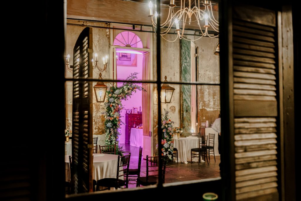 Looking through a window at a Spring wedding floral display in a doorway of Latrobe's, gas lanterns on the wall and a chandelier hanging from the ceiling.