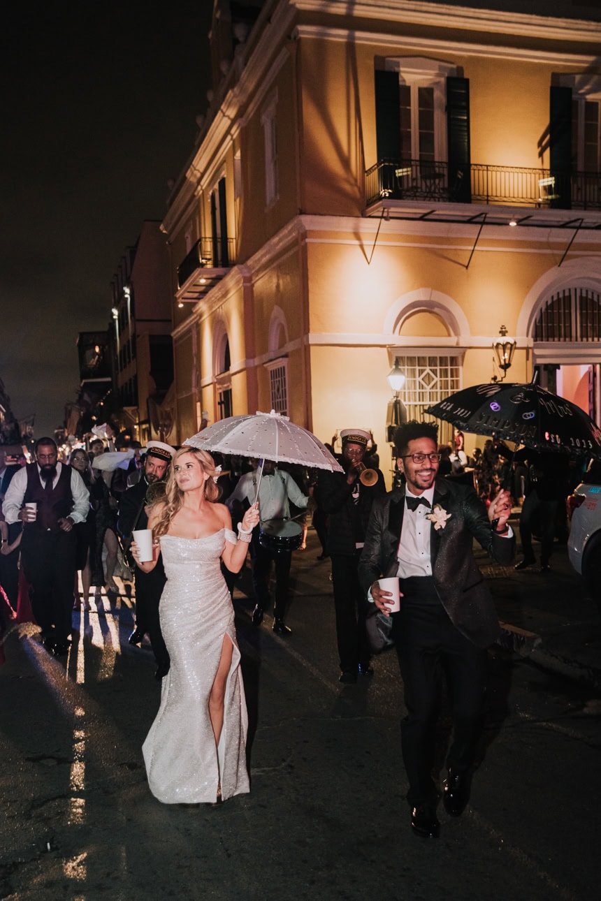 Bride and groom walking in a second line parade in New Orleans at night with Latrobe's in the background.