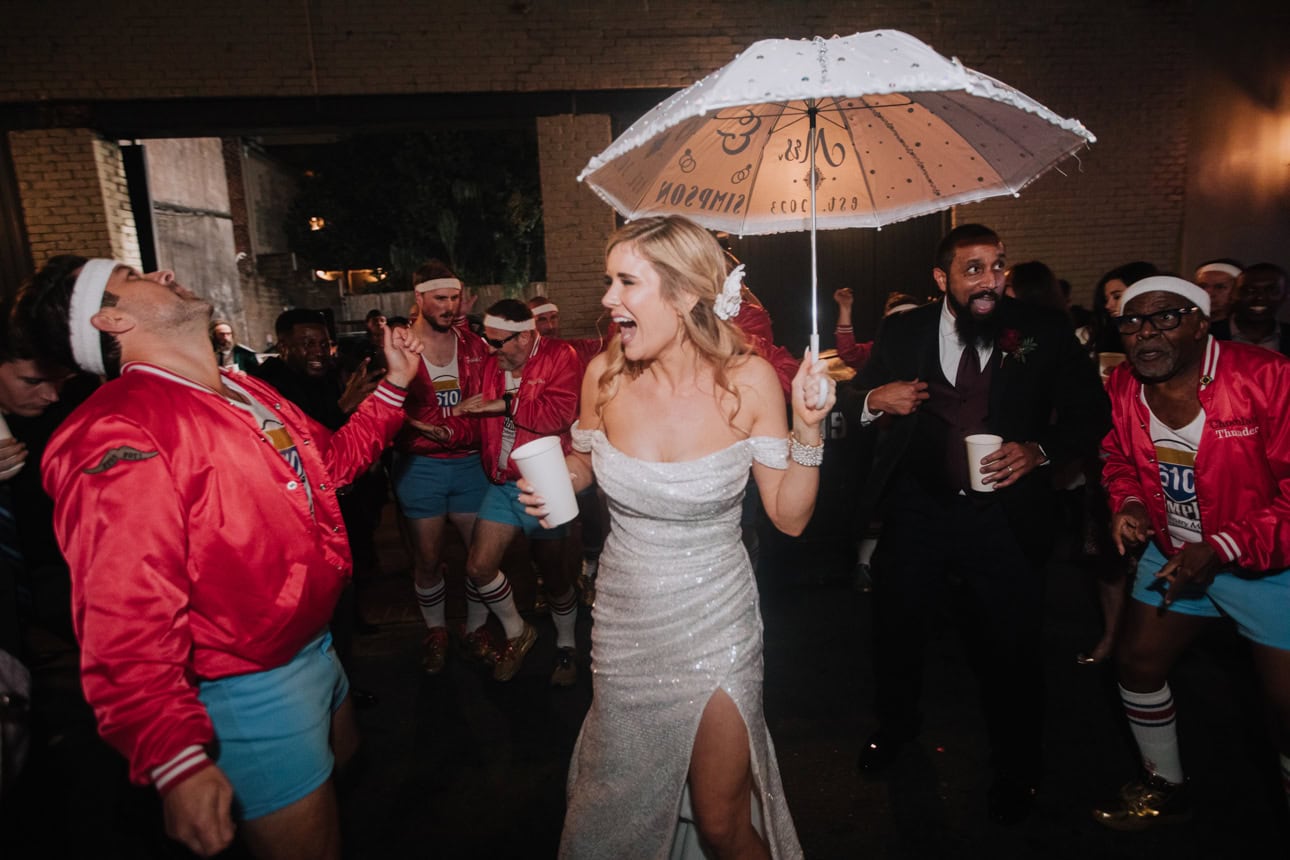 A bride dances in the street with an umbrella with a member of the New Orleans' 610 Stompers.