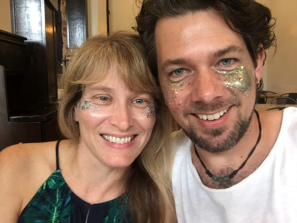Liz King and Matt Foster smiling at the camera wearing glitter on their faces.