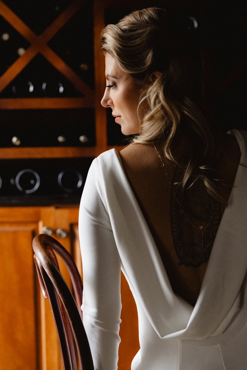 the profile of a beautiful bride her hair cascading down her back. she is sitting in a chair.