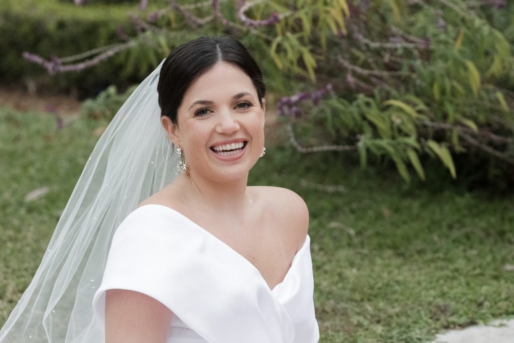 Beautiful bride with dark hair and sparkling earrings, captured in a natural garden environment.
