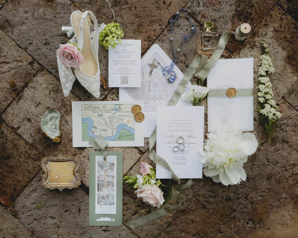 Elegant New Orleans wedding flat lay featuring invitation, flowers, rings, rosary, perfume, and wedding accessories.
