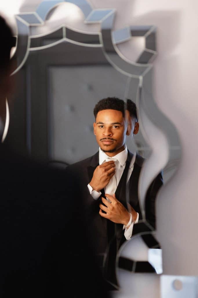 Groom adjusting his tie in front of a decorative mirror, portrait shot for wedding photography.