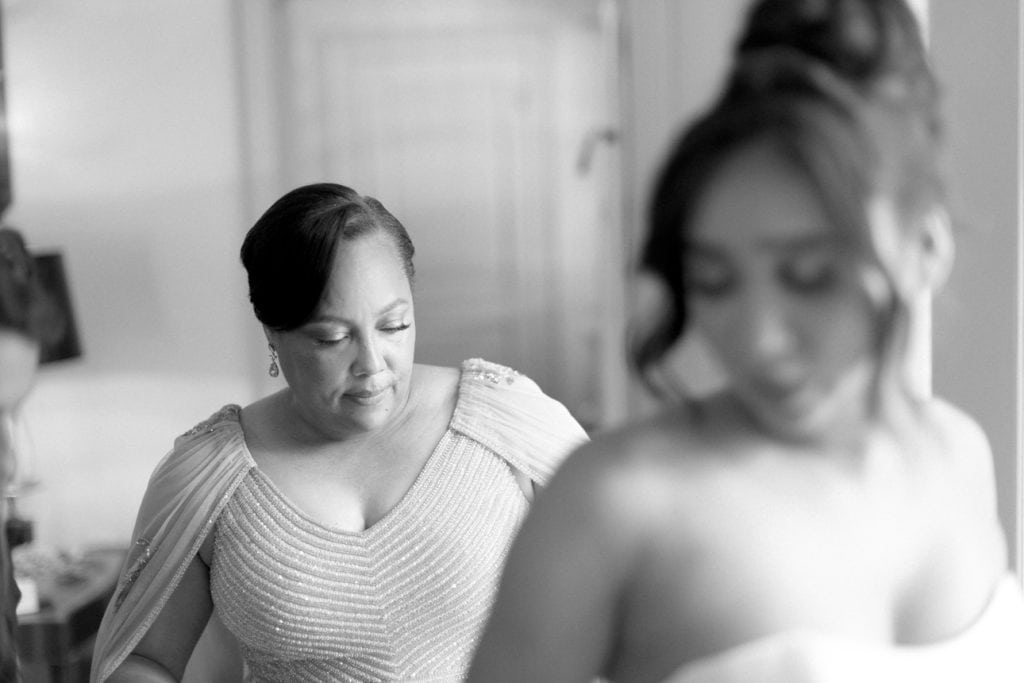 Mother assisting bride with wedding dress, emotional moment, black and white wedding photography.