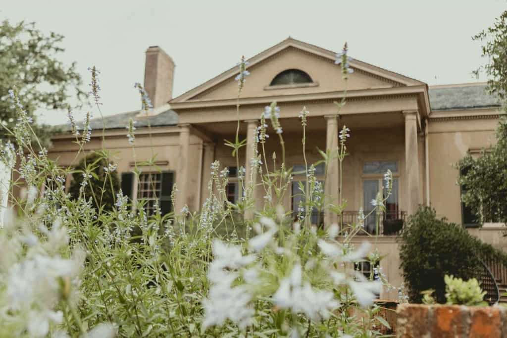 Old mansion with lush garden and blooming flowers in the foreground.