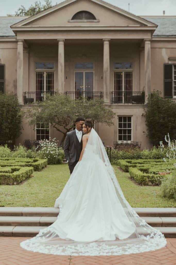Wedding couple outdoors at historic mansion with lush garden backdrop.
