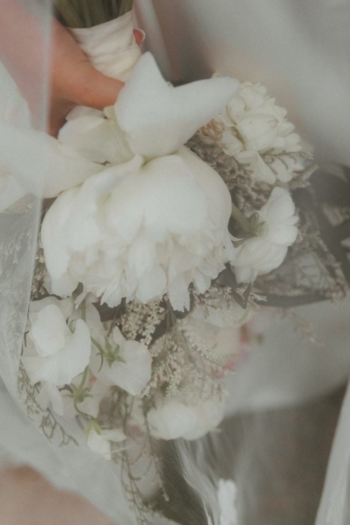 Elegant white peony bouquet with delicate greenery for a wedding celebration.