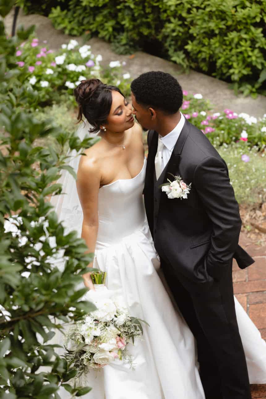 Elegant bride and groom share a kiss outdoors in a lush garden setting.