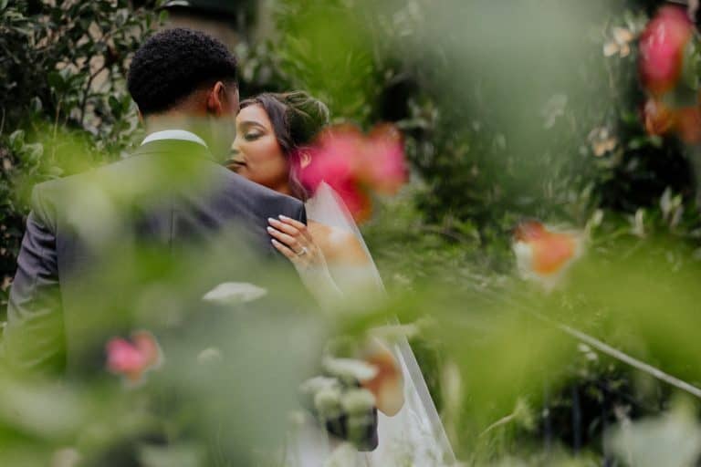 Close-up of bride and groom kissing with greenery around.