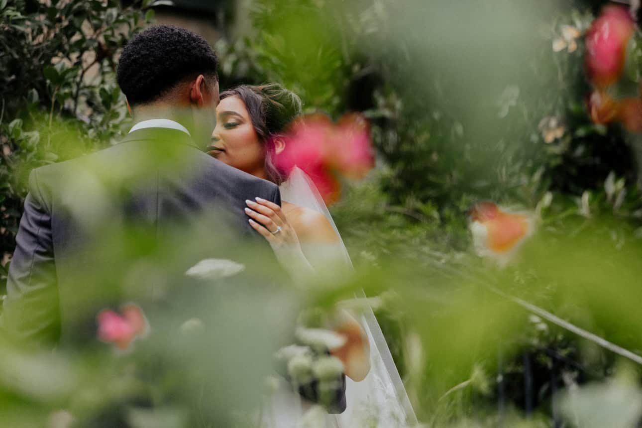 Close-up of bride and groom kissing with greenery around.