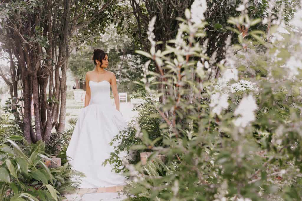 Beautiful bride in wedding dress surrounded by greenery and foliage.