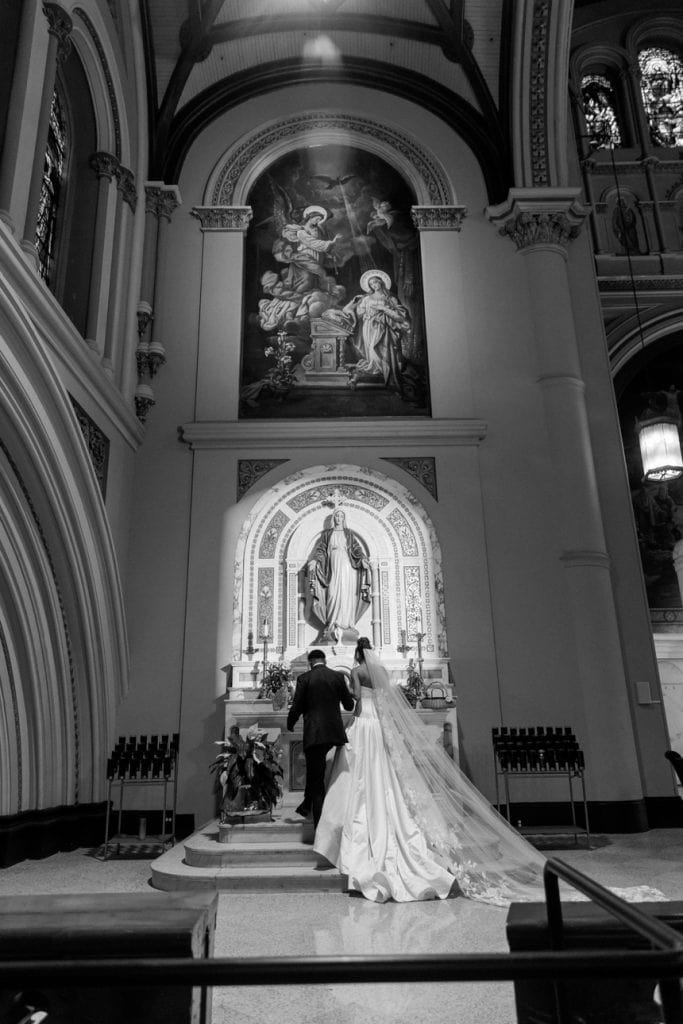 Wedding couple in front of religious statues in a stunning church setting.