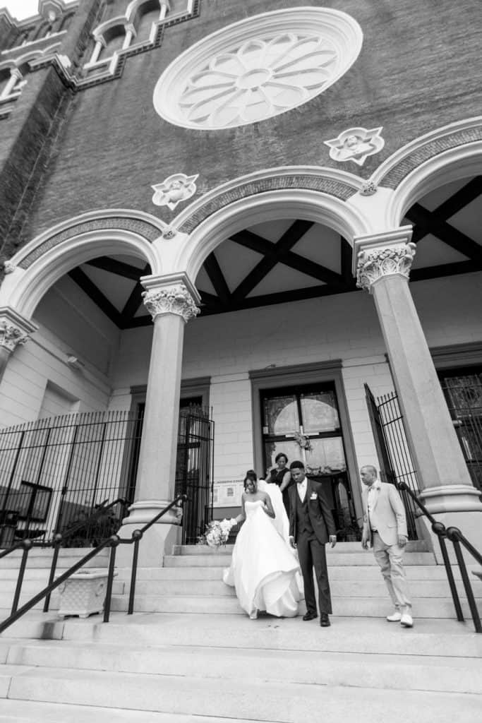 Bride and groom walking down church stairs after wedding ceremony in black and white.