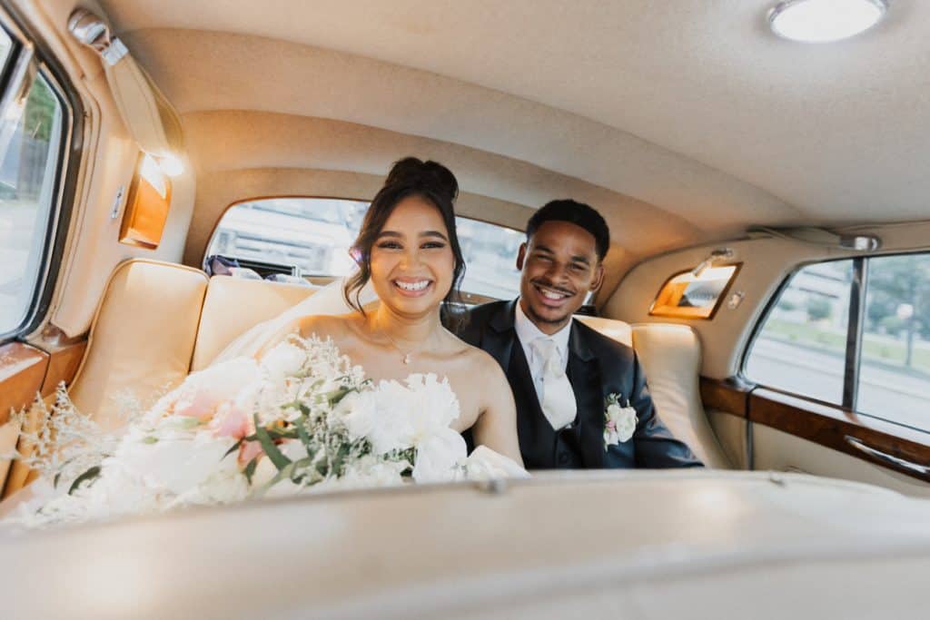 Joyful bride and groom inside classic vehicle packed with love.