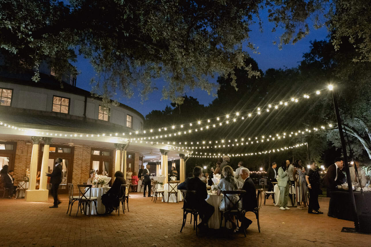 Beautiful evening wedding reception in New Orleans with guests dining outdoors under twinkling string lights.