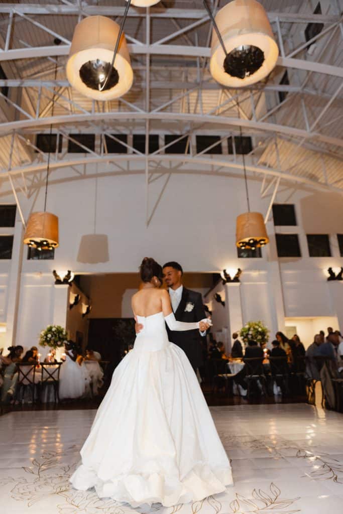 Wedding couple dancing during reception at stylish New Orleans venue Lighting fixtures and social guests visible.
