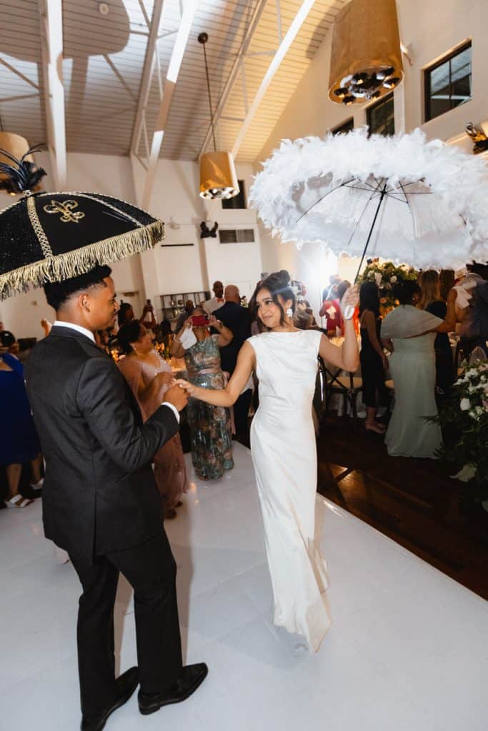 A bride and groom dance at a vibrant New Orleans wedding reception, holding ornate umbrellas in a stylish indoor venue.