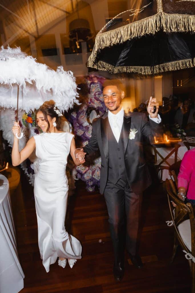 Happy wedding couple dancing with umbrellas indoors in New Orleans celebration.