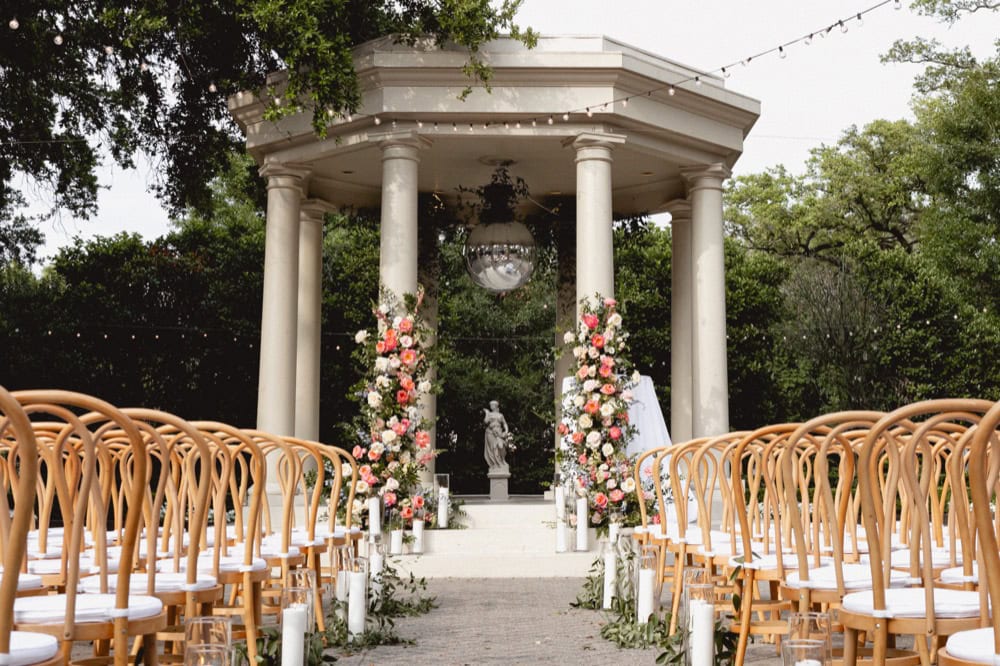 Outdoor wedding ceremony with floral decorations and a historic pavilion backdrop.