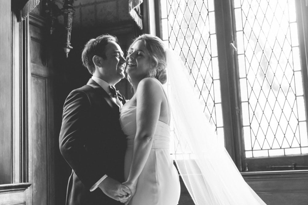 Wedding couple smiling and holding hands in a historic New Orleans venue, the Elms Mansion, with stained glass windows.