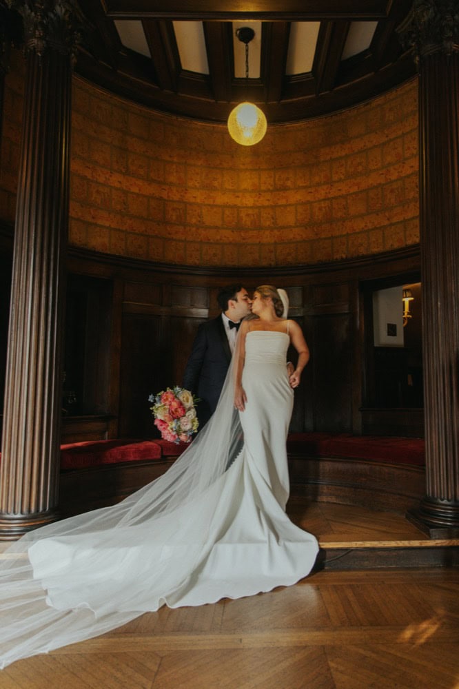 Bride and groom sharing a kiss at the Elms Mansion, a historic New Orleans venue, with wooden accents.