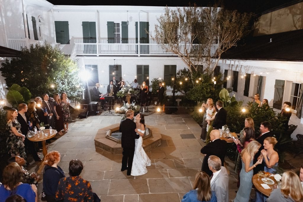 Romantic couple sharing their first dance surrounded by friends and family under string lights at the BK House.