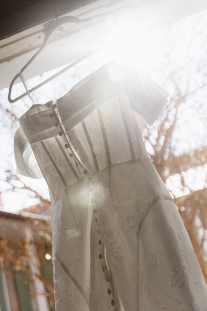 Beautiful wedding gown displayed outdoors with sunlight filtering through trees.