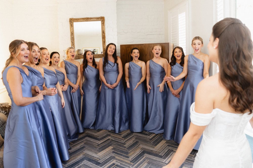 Bridesmaids in blue dresses excitedly gather before the bride on her special day.
