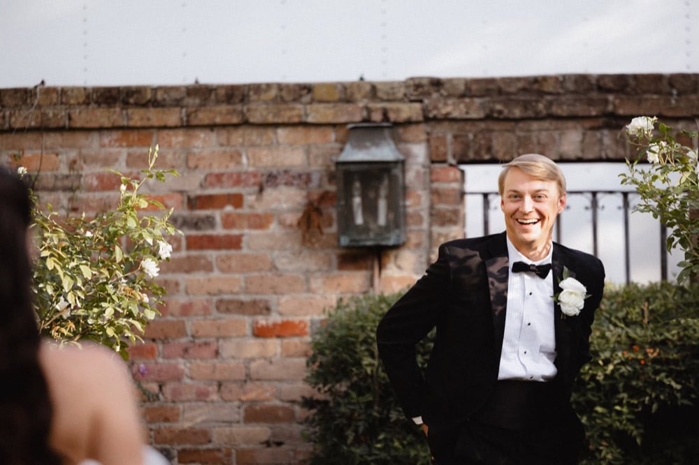 Groom reacts with a smile as he sees his bride for the first time in the courtyard of the BK House and Gardens in New Orleans.