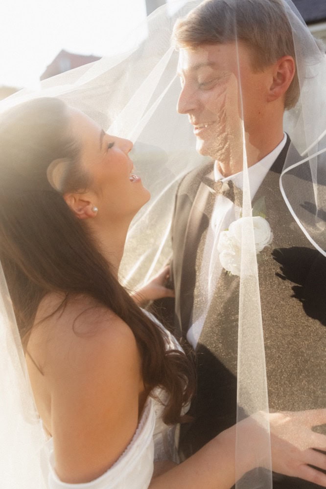 Bride and groom sharing a joyful moment under a veil outdoors.