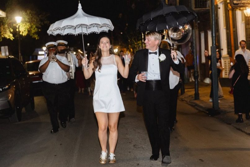 Wedding couple walking in New Orleans at night with umbrellas, celebrating.