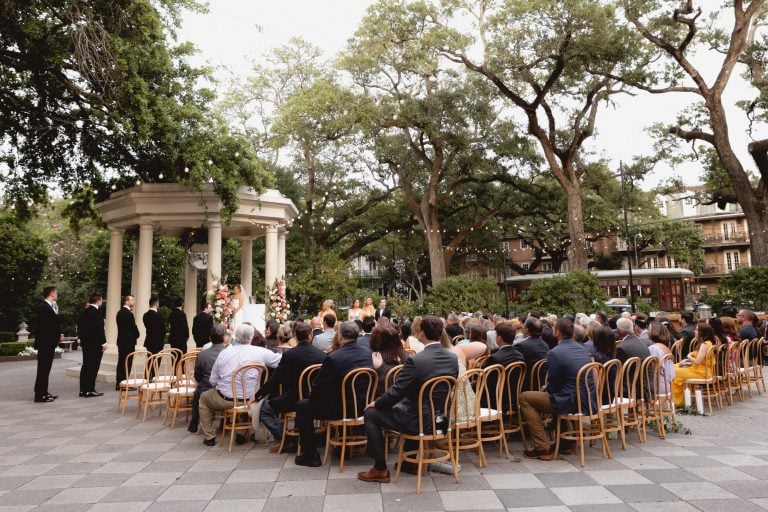Wedding ceremony at The Elms Mansion in New Orleans with guests seated outdoors under large trees with the streetcar going by in the background.