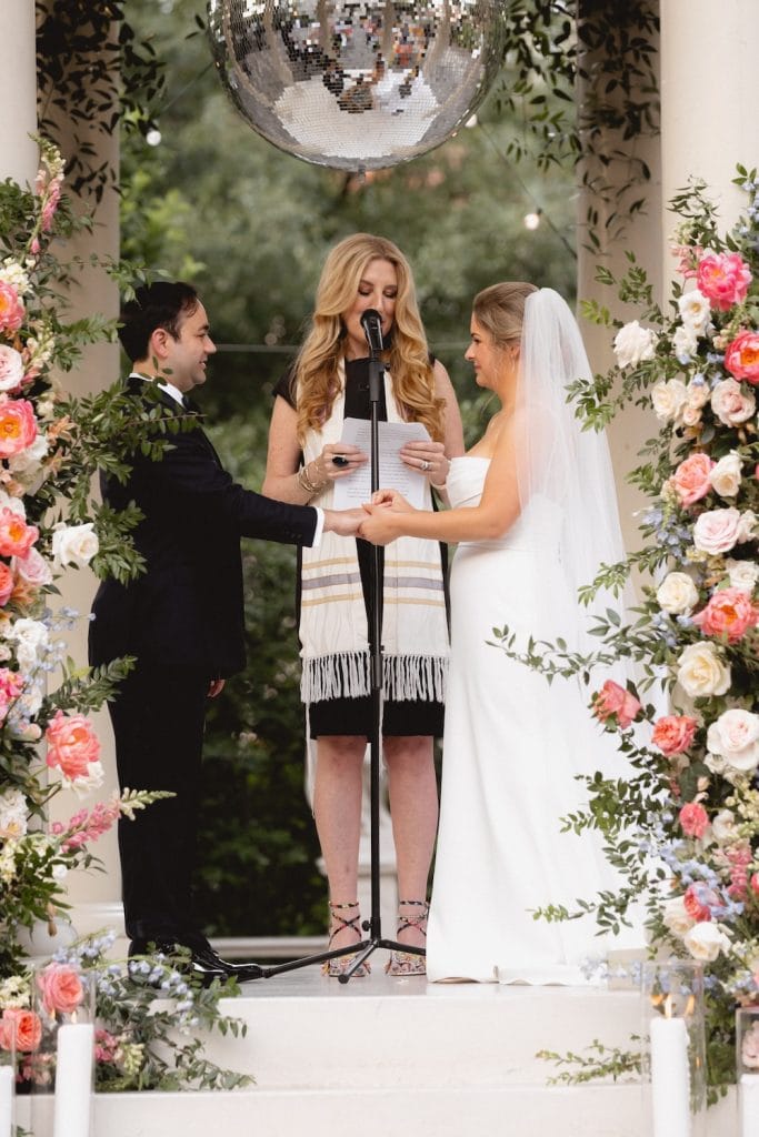 Romantic wedding ceremony outdoors with floral arch and officiant at The Elms Mansion in New Orleans.