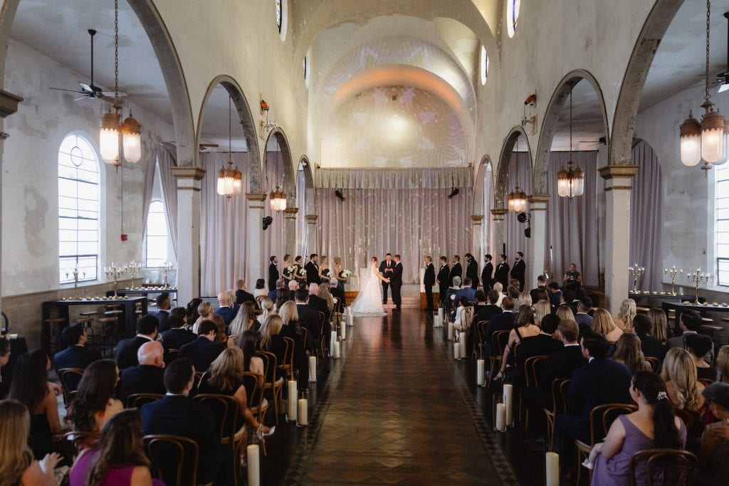 Elegant New Orleans wedding ceremony in the Marigny Opera House with guests seated and couple exchanging vows.