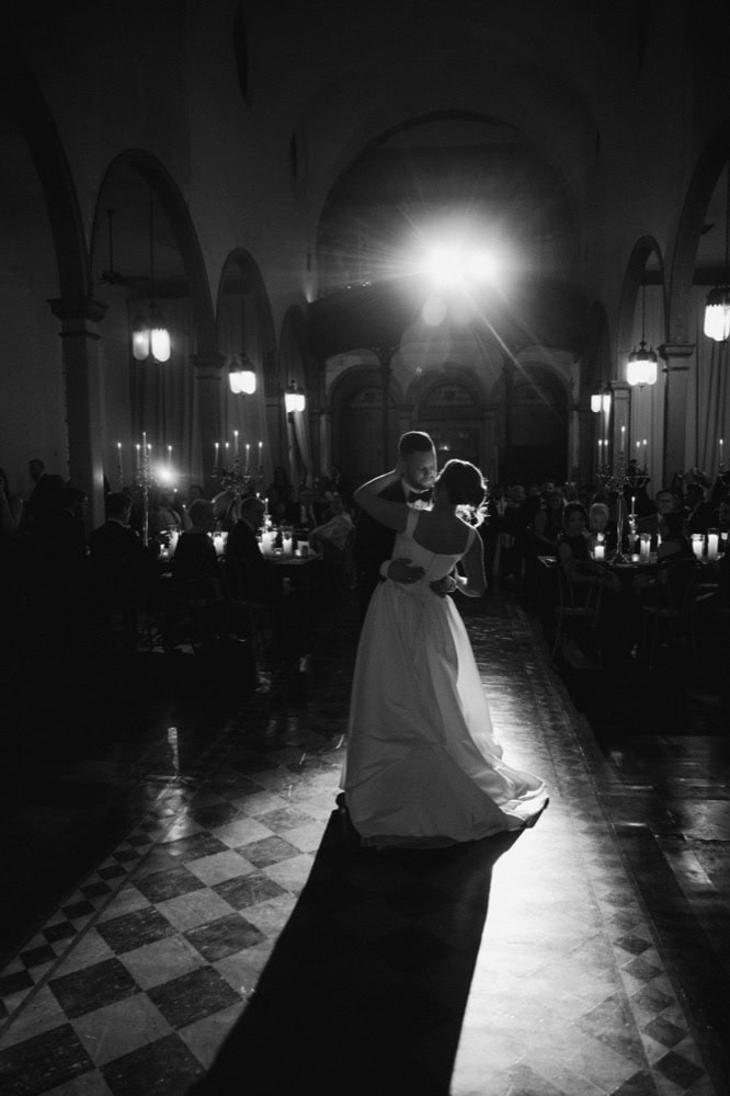 Bride and groom sharing their first dance in a grand ballroom with dramatic lighting.
