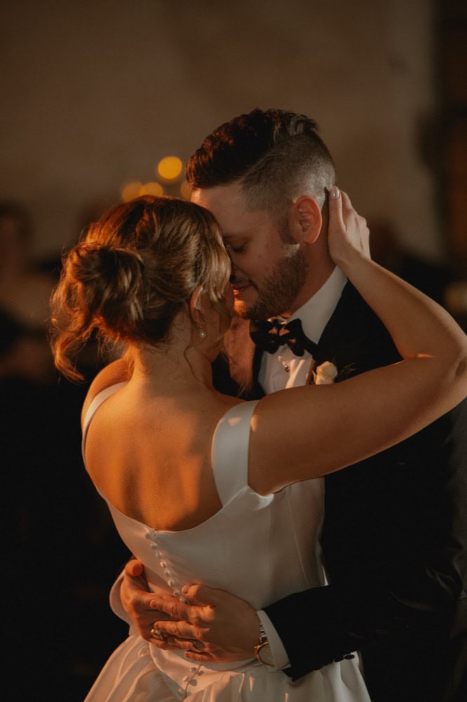 Romantic couple's first dance at wedding reception in warm lighting.