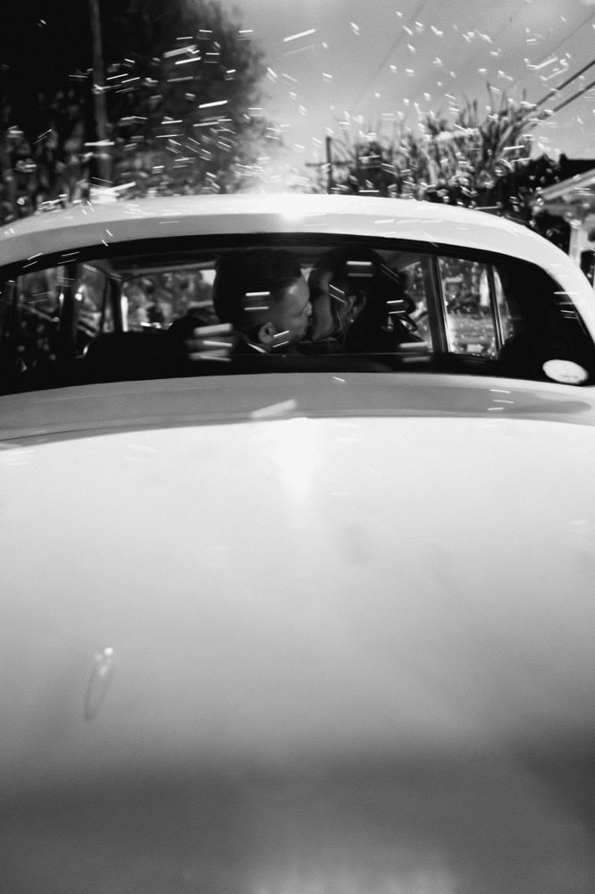 Bride and groom kiss in the back of a vintage Rolls Royce as they exit their wedding, the air filled with bubbles.