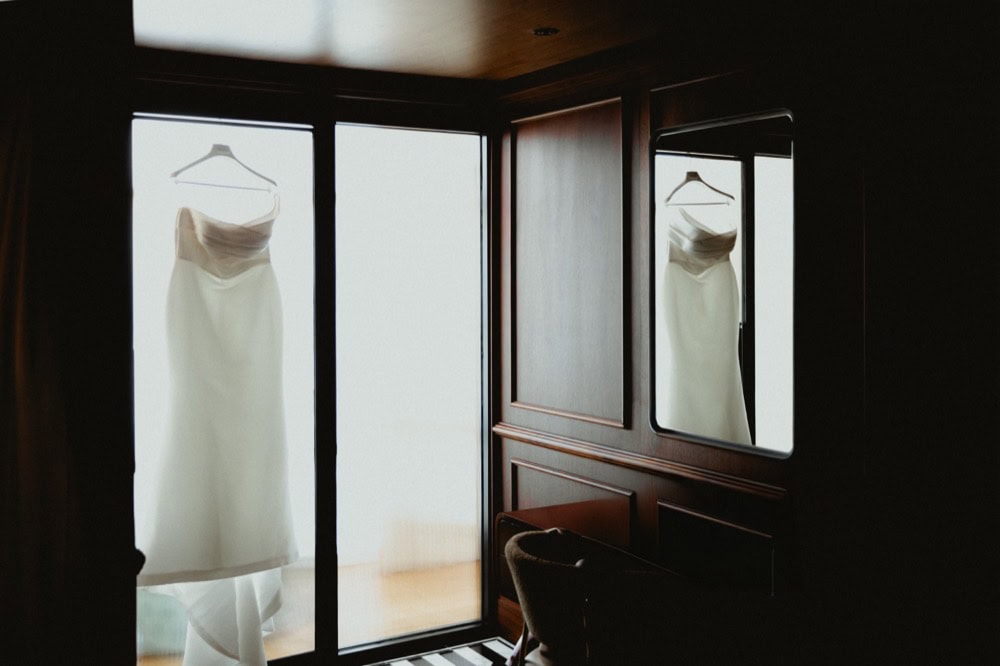 White strapless wedding gown hangs in a glass doorway.