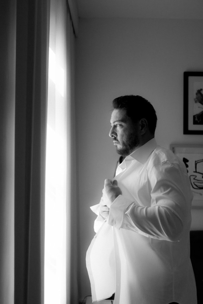 A groom buttons his white shirt while he gets ready for his wedding day in New Orleans.
