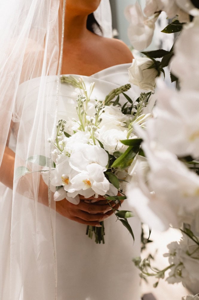 A bride holding flowers that are white with orchids.