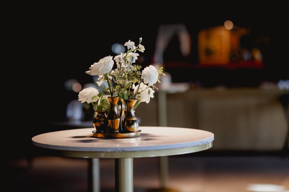 White flowers in small gold vases on a white table.