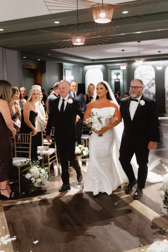 The bride is escorted down the aisle while guests look on at a New Orleans wedding.
