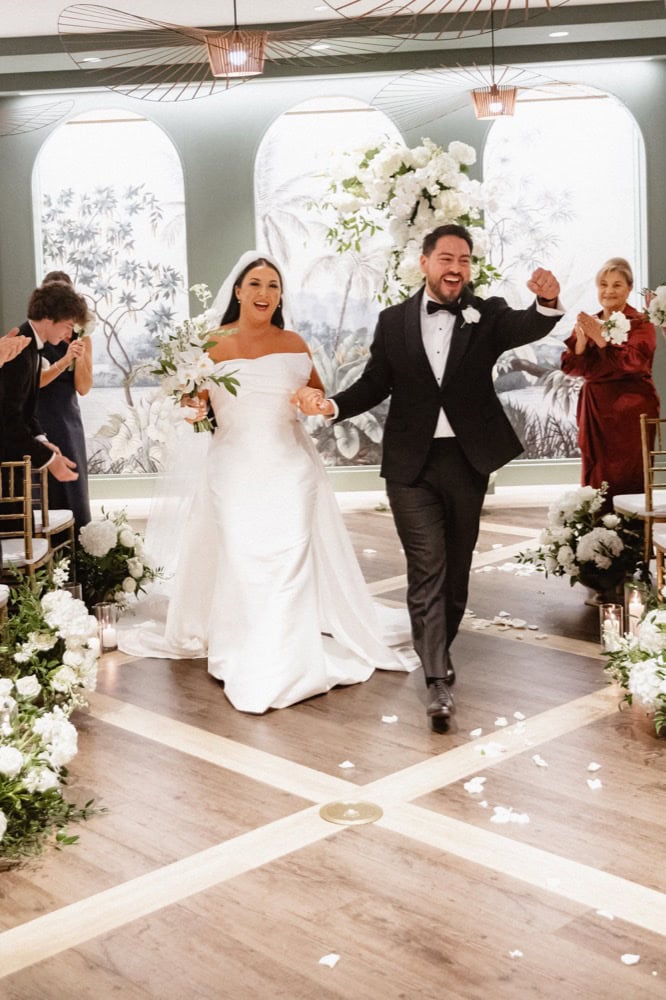 Bride and groom cheer at their wedding at the Virgin Hotel in New Orleans as they come down the aisle just wed.