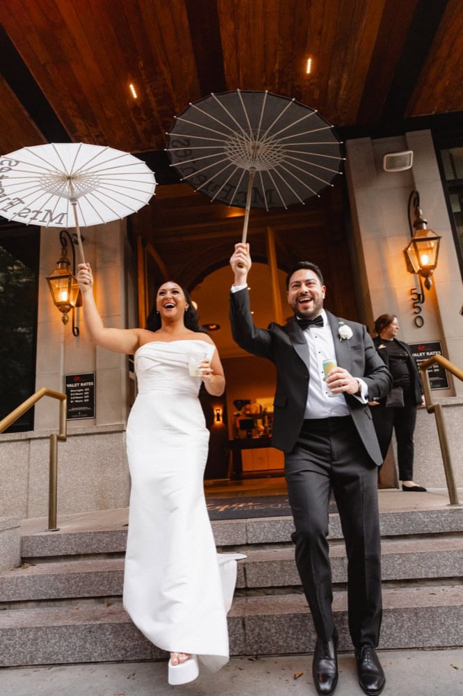 Bride and groom cheer and hold umbrellas at their wedding at the Virgin Hotel in New Orleans as they exit to begin their second line parade.