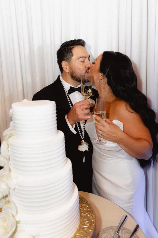 The bride and groom share a kiss and toast with champagne by their wedding cake at the Virgin Hotel in New Orleans.