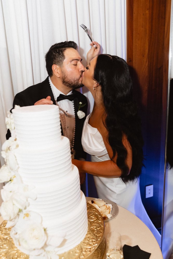 The bride and groom share a kiss by their wedding cake at the Virgin Hotel in New Orleans.